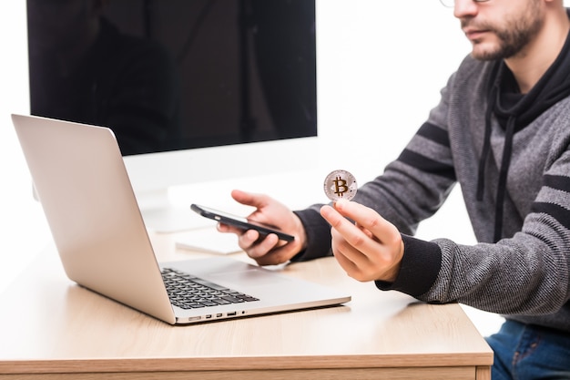 Free photo close up of hands of man at working place woth laptop and monitor screen, holding phone and bitcoin