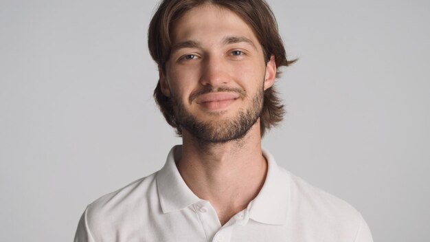 Close up handsome bearded guy looking calm at camera over white background Beautiful male model posing in studio