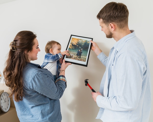 Free photo close-up of happy couple with their baby toddler fixing picture frame on wall