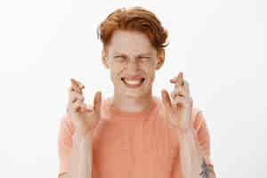 Free photo close-up of hopeful redhead man student cross fingers good luck, making wish