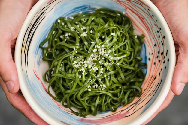 Free Photo close-up of human hand holding bowl of chuka seaweed salad with sesame seeds