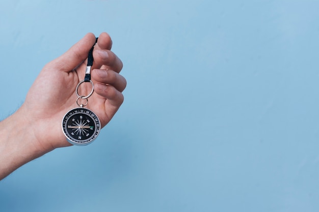 Free photo close-up of human hand holding navigational compass on blue backdrop