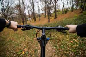 Free photo close-up image of cyclist man hands on handlebar riding mountain bike on trail in autumn park