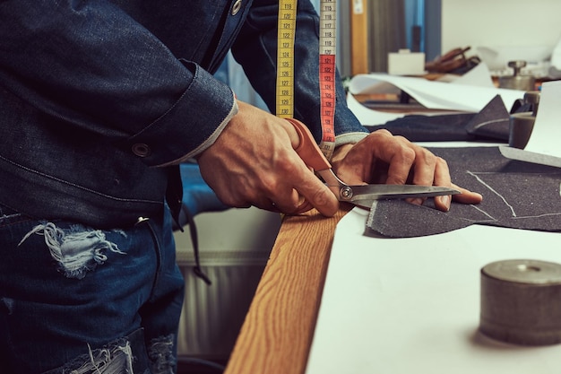 Free photo close-up image of a tailor cutting dark cloth at a sewing workshop.