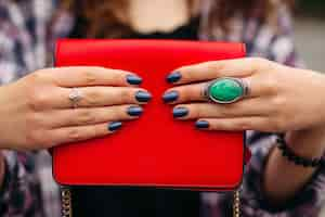 Free photo close-up of incognito woman with elegant dark nails on manicured fingers with rings wearing red compact crossbag of bright red color.