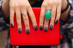 Free photo close-up of incognito woman with elegant dark nails on manicured fingers with rings wearing red compact crossbag of bright red color.