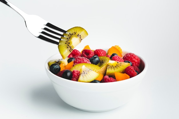 Close-up kiwi on fork with bowl of fruit