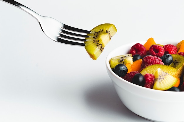 Free photo close-up kiwi on fork with bowl of fruit