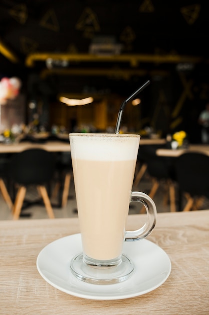 Free photo close-up of latte coffee cup with straw and saucer on wooden desk