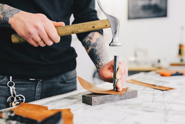 Free Photo close up of a leather craftsman working with leather using hammer. 