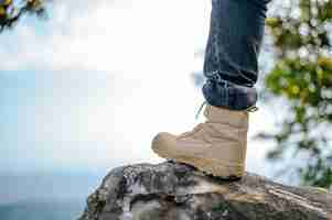 Free photo close up leg of hiking man in jeans with trekking sneakers placed on rocky mountain peak in the natural forest blue sky on background copy space