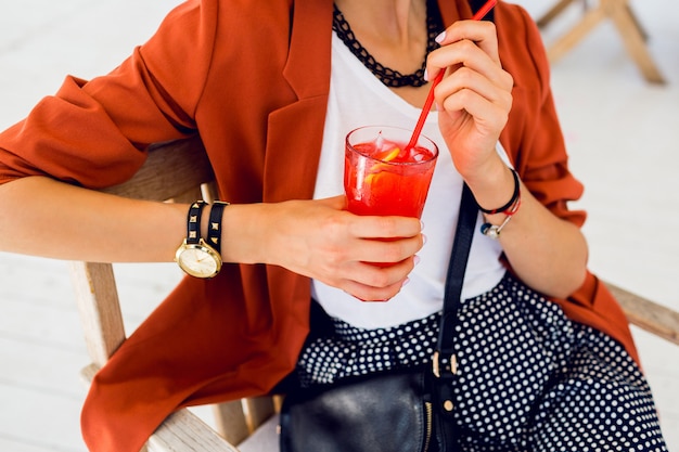 Free photo close up lifestyle  portrait of cute stylish young woman posing outdoor, sitting in summer cafe and drinking  exotic cocktail, sea background. bright colors. vacation mood. smiling and have fun.