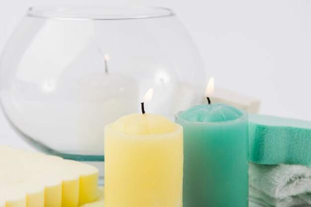 Close-up of lighted yellow and green candle with sponges over white background