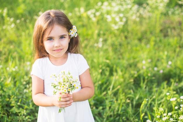 Close-up of little girl holding bunch of white flowers in the meadow