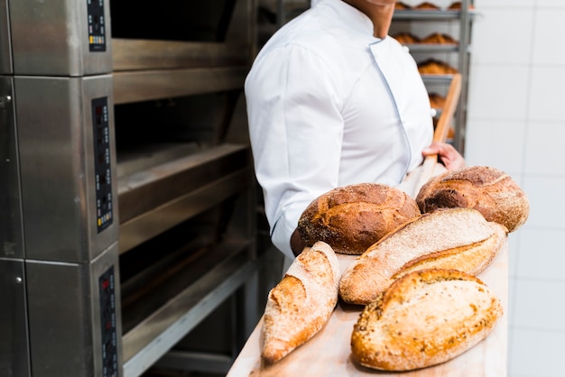 Close-up of a male baker holding fresh baked bread on wooden shovel from the oven