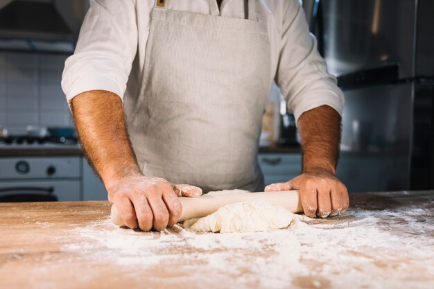 Close-up of male baker's hand flattening dough with rolling pin