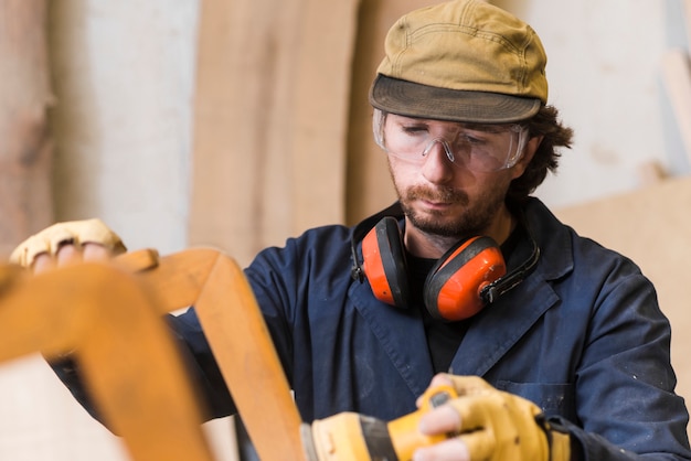 Free Photo close-up of a male carpenter wearing safety glasses and ear defender around his neck using electric sander