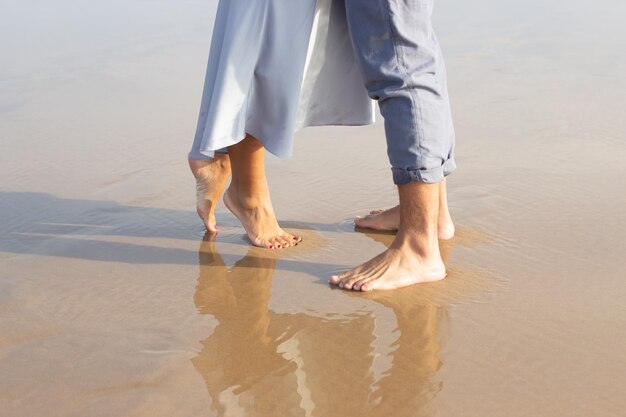 Close-up of male and female bare feet on wet sand.  Man and woman walking at beach with a waves edge foaming gently beneath. Vacation, happiness concept