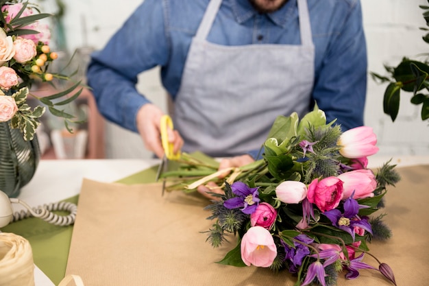 Close-up of male florist cutting the paper for wrapping the flower bouquet