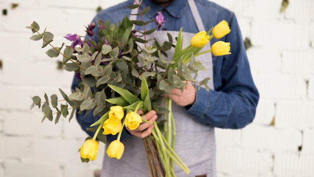 Free Photo close-up of male florist holding yellow tulips and twigs in hand