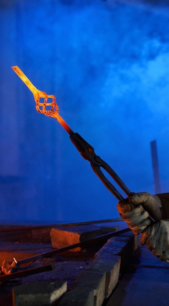 Free Photo close up of male hands in safety gloves holding forceps with heated shaped steel professional blacksmith working with molten metal at forge concept of handwork and industry