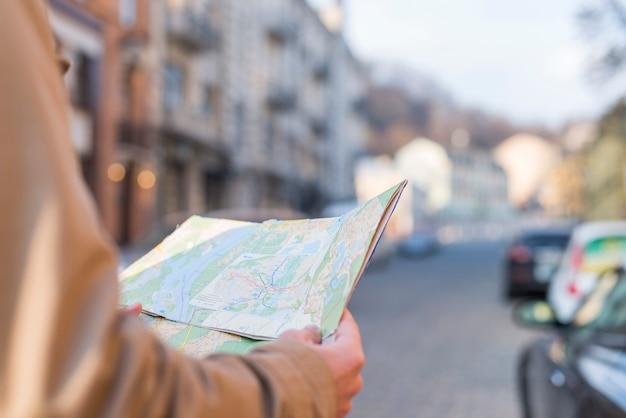 Close-up of male traveler holding map in hand standing on city street