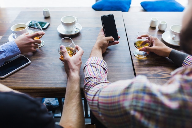 Close-up of males hand holding glasses of drinks using mobile phone