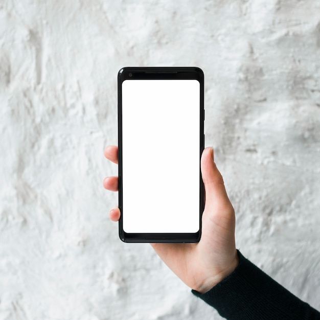 Free Photo close-up of a man holding a blank smart phone screen against white concrete wall