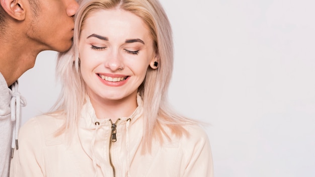 Close-up of man kissing her smiling girlfriend against white background