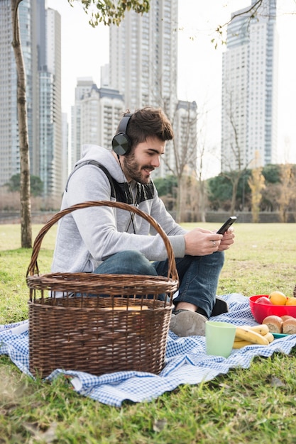 Close-up of a man listening music on headphone using mobile phone at picnic