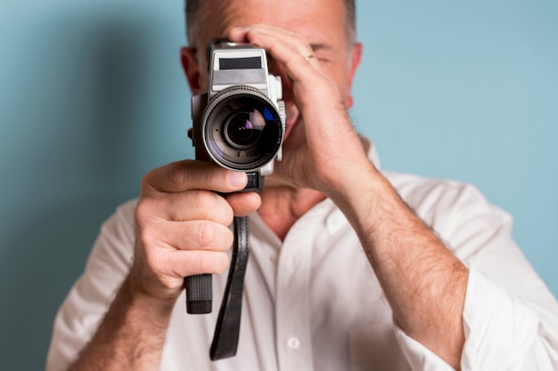 Free Photo close-up of a man looking through 8mm film camera against blue backdrop