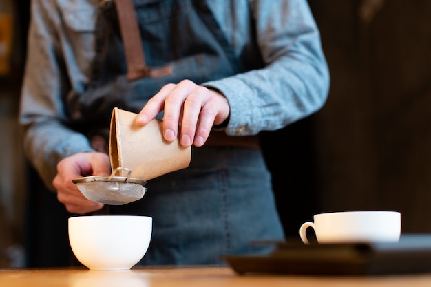 Close-up of man pouring coffee in cup through sieve