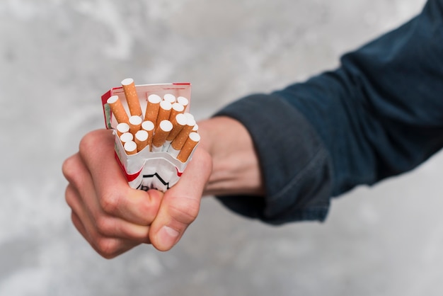 Close-up of man's hand crushing cigarettes box