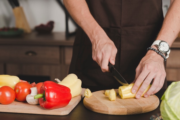 Free Photo close-up of man's hand cutting bellpepper with knife on chopping board