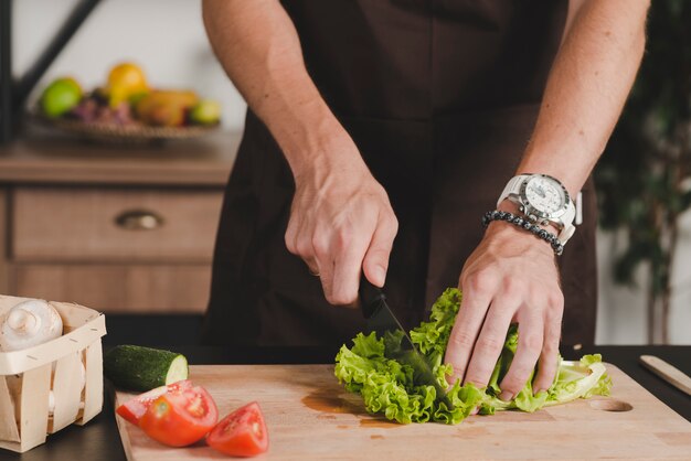 Close-up of man's hand cutting lettuce with knife on chopping board