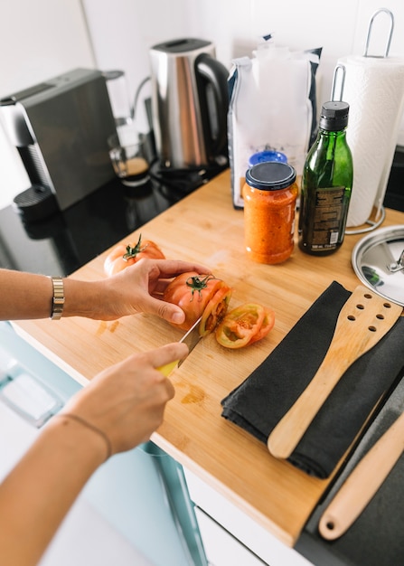 Close-up of man's hand cutting slices of tomato on kitchen counter