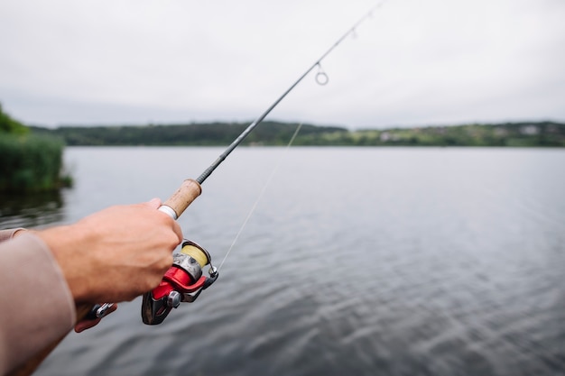 Close-up of man's hand holding fishing rod over the lake