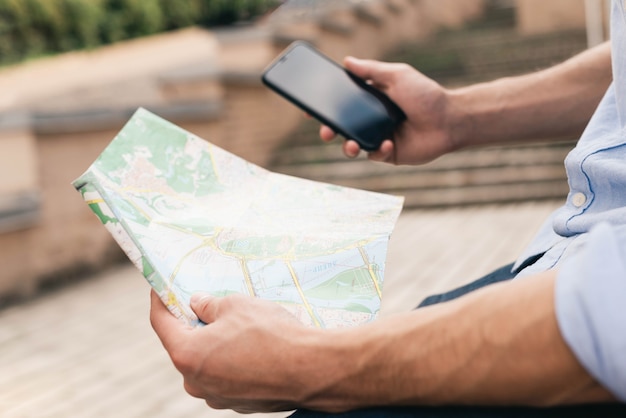 Free photo close-up of man's hand holding map and cell phone at outdoors