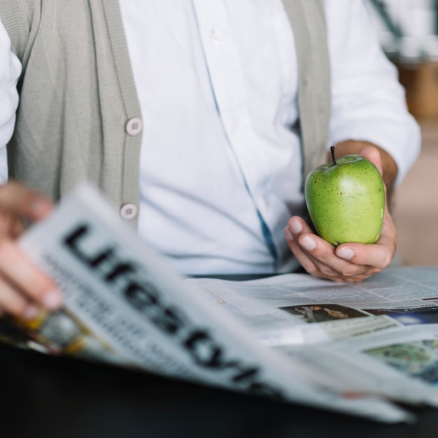 Free photo close-up of man's hand holding newspaper and green apple