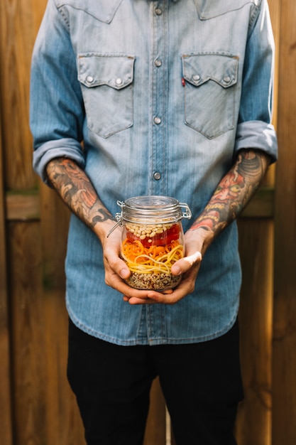 Close-up of a man's hand holding pasta salad in mason jar