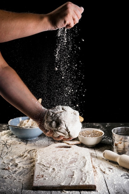 Free photo close-up of man's hand sprinkling the flour on the dough