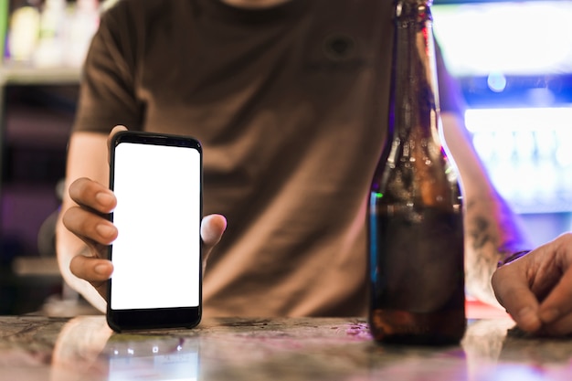 Free photo close-up of man showing blank white mobile screen with beer bottle on table