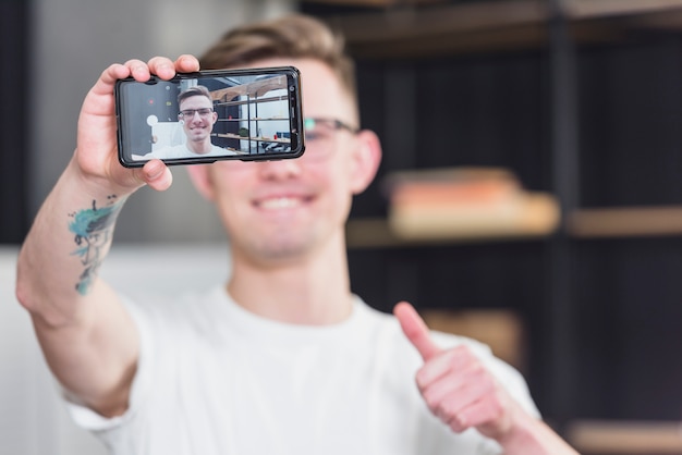 Free photo close-up of a man taking selfie on mobile phone showing thumb up sign