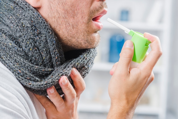 Free photo close-up of a man wearing gray scarf around his neck using a spray to treat sore throat