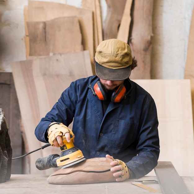 Close-up of a man with ear defender around his neck using sander for smoothing wooden block