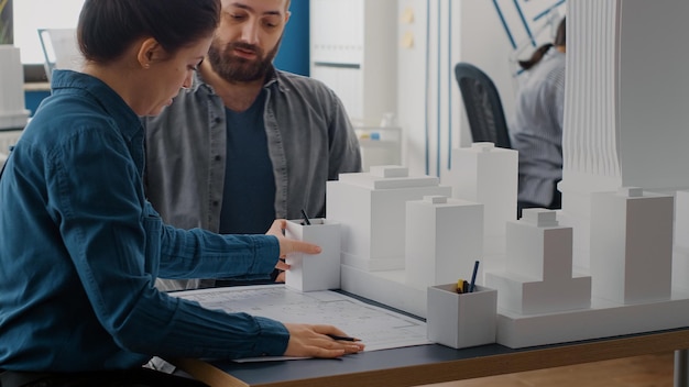 Free Photo close up of man and woman designing blueprints plan, analyzing building model. team of people working on construction design with industrial sketch and maquette for urban project.