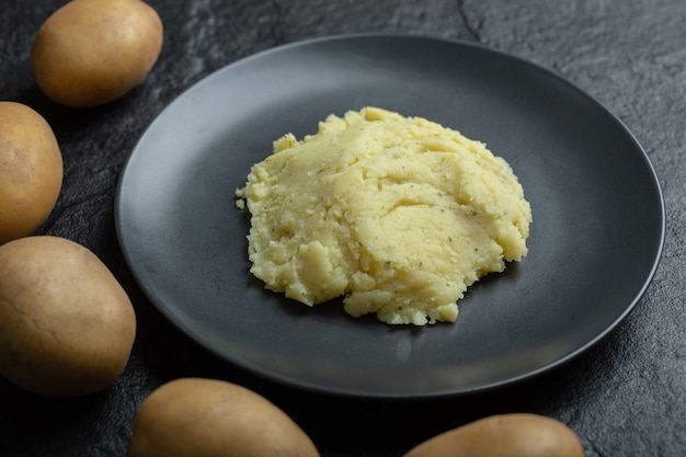 Free photo close up of mashed potato on a plate, and fresh potatoes around it.