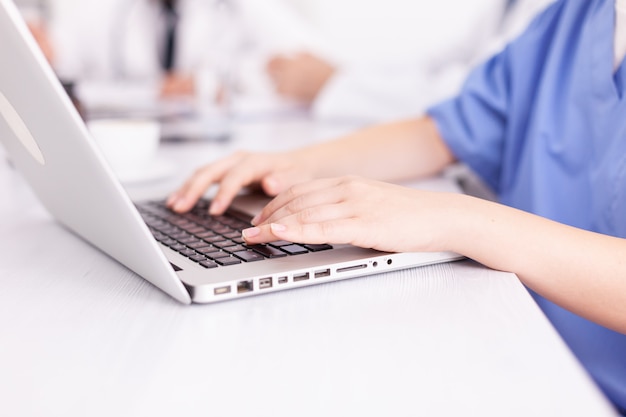 Close up of medical nurse typing on laptop during healtchare meeting with coworkers in hospital boardroom. Clinic expert therapist talking with colleagues about disease, medicine professional