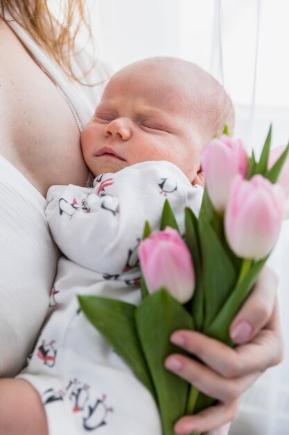 Close-up of mother holding sleeping baby and pink tulip flowers