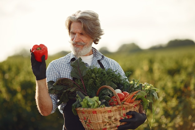 Free photo close up of old farmer holding a basket of vegetables. the man is standing in the garden. senior in a black apron.